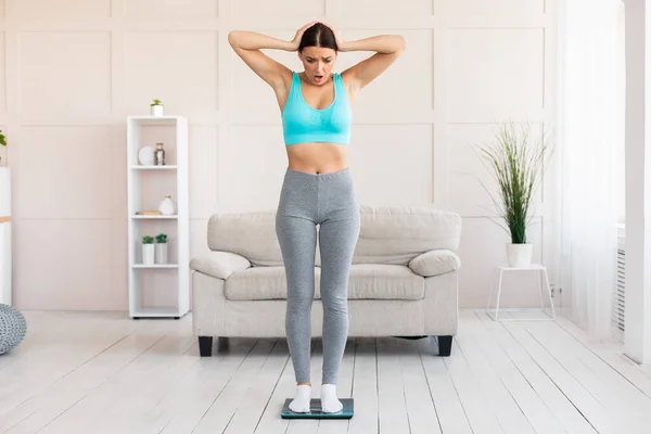 Donna scioccata in piedi su bilance di peso guadagnando chilogrammi a casa — Foto Stock