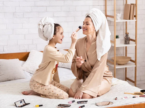 Madre e hija usando toallas de baño y divirtiéndose con maquillaje en la cama —  Fotos de Stock