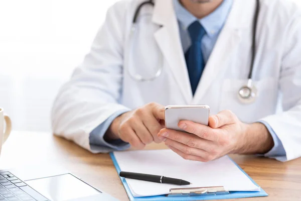 Medico utilizzando smartphone sul posto di lavoro, messaggistica con il paziente — Foto Stock