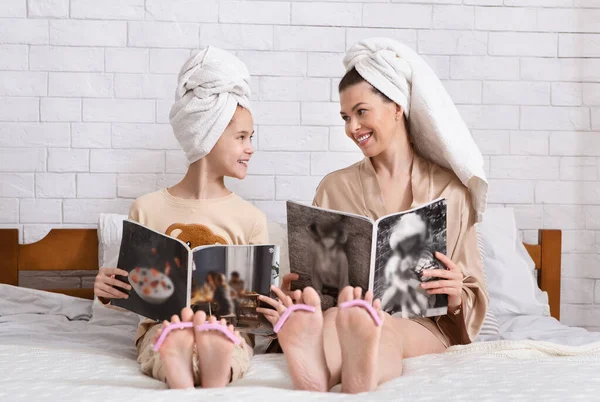 Attraktive junge Frau und ihre Teenager-Tochter lesen Modezeitschriften und tun Nägel nach dem Bad im Schlafzimmer — Stockfoto