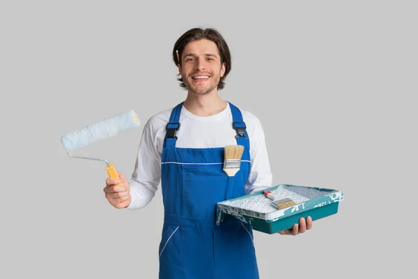 Servicios de renovación. Pintor sonriente en uniforme con herramientas de pintura en las manos — Foto de Stock