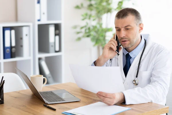 Mužský lékař s lékařskou zprávou volá na kliniku — Stock fotografie