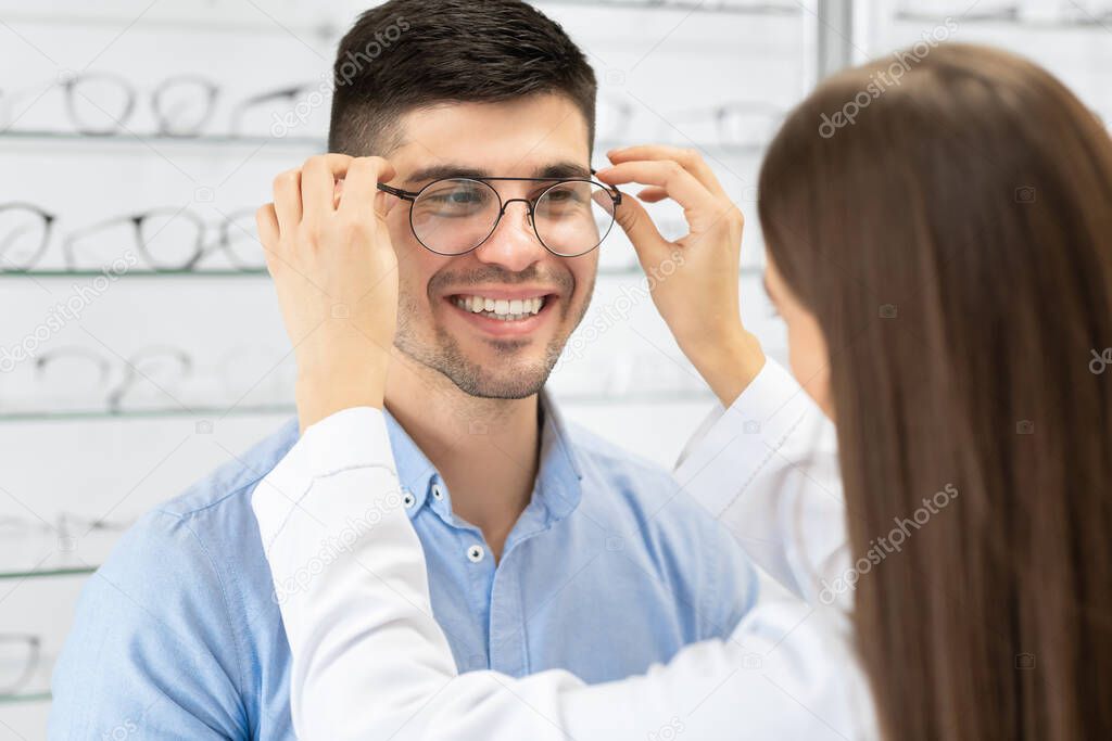 Optometrist helping young man to choose correction glasses