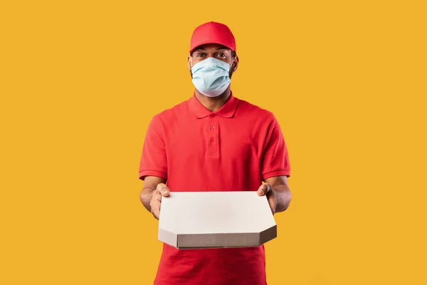 Courier Guy segurando caixa de pizza vestindo máscara em fundo amarelo — Fotografia de Stock