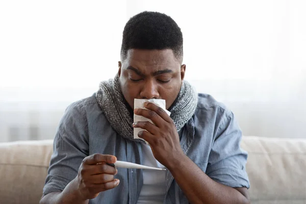 Alta Temperatura. Doente em quarentena homem sentado com termômetro em mãos em casa — Fotografia de Stock