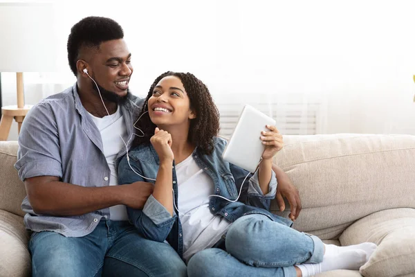 Μαύρο ζευγάρι μοιράζονται ακουστικά ακούγοντας μουσική σε ψηφιακό tablet στο σπίτι — Φωτογραφία Αρχείου