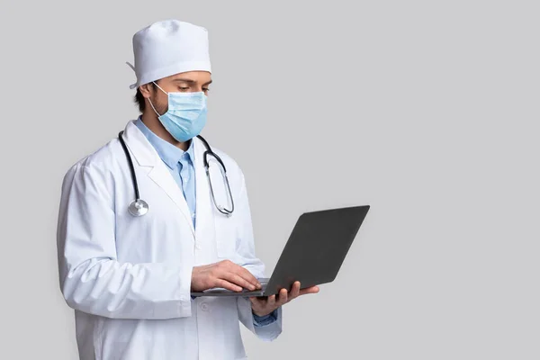 Koruyucu maskeli doktor laptoptaki hastalara danışıyor. — Stok fotoğraf