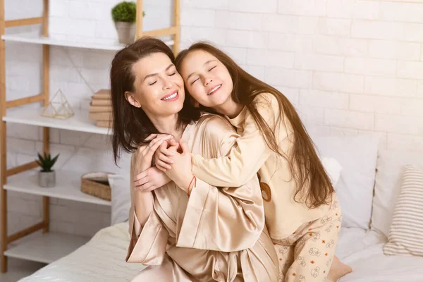 Szczęśliwych rodzinnych chwil. Nastolatka przytula mamusię, wyrażając miłość w sypialni — Zdjęcie stockowe