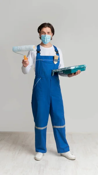 Muž malíř nosit lékařskou masku a držet malířské nástroje v rukou — Stock fotografie