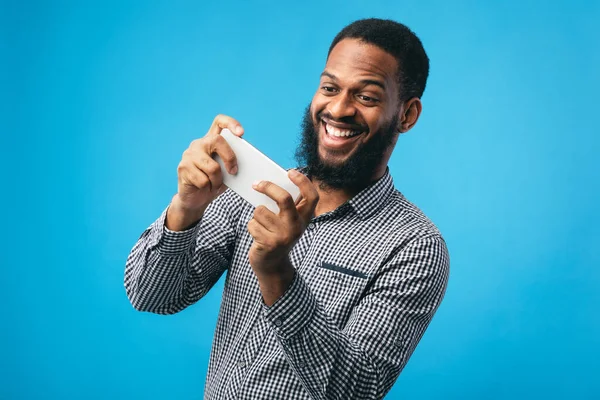Emocionado hombre afro utilizando el teléfono móvil sobre fondo azul — Foto de Stock