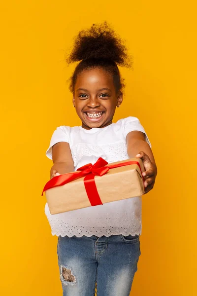 Cute shy little african girl giving gift box at camera — Stock Photo, Image