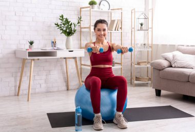 Evde dayanıklılık eğitimi. Milenyum kızı oturma odasında halterlerle ve spor salonuyla egzersiz yapıyor.