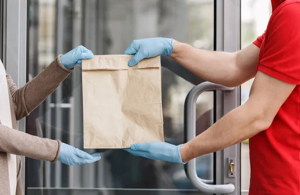 Courier em luvas de borracha entrega saco de papel para o cliente em casa . — Fotografia de Stock