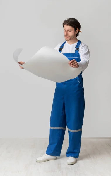 Full-length portrait of young construction engineer checking draft or building plan — Stock Photo, Image