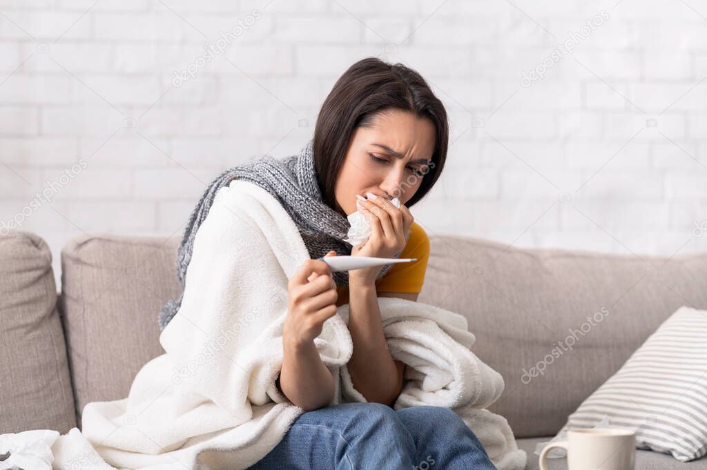 Sick woman suffering from bad infection with high fever, looking at thermometer at home