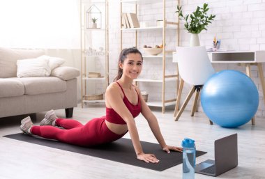 Genç çekici yoga eğitmeni evde dizüstü bilgisayarla ders veriyor.