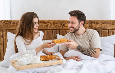 İki konsept için romantik kahvaltı. Kız, ayçöreğini yatakta erkeğe verir.