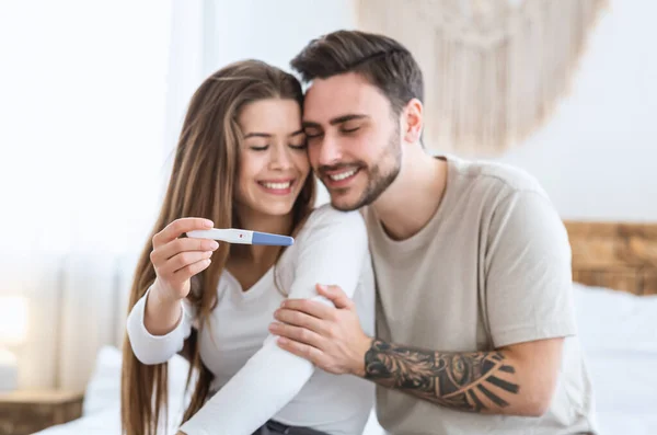 Καλά νέα. Χαρούμενος άντρας αγκαλιάζει κορίτσι και δείχνει θετικό τεστ εγκυμοσύνης — Φωτογραφία Αρχείου