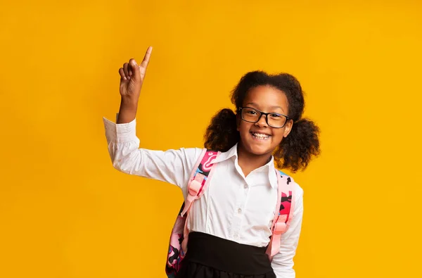 Usmívající se školačka ukazující prstem nahoru s otázkou přes žluté pozadí — Stock fotografie