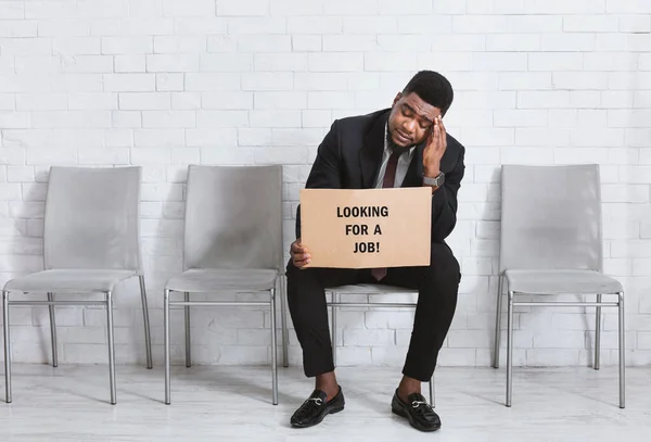 Africano americano em terno de negócios segurando sinal à procura de emprego enquanto espera para entrevista no escritório. Espaço de cópia — Fotografia de Stock