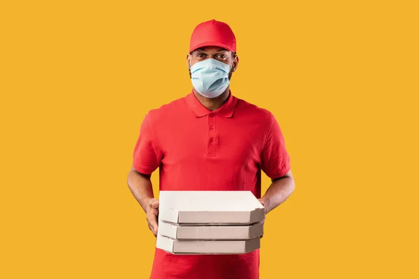 Homem africano entregando pizza de restaurante vestindo máscara, fundo amarelo — Fotografia de Stock
