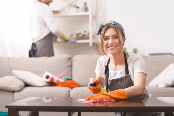 Donna pulizia polvere da tavolo mentre il suo fidanzato pulire scaffali su sfondo — Foto Stock