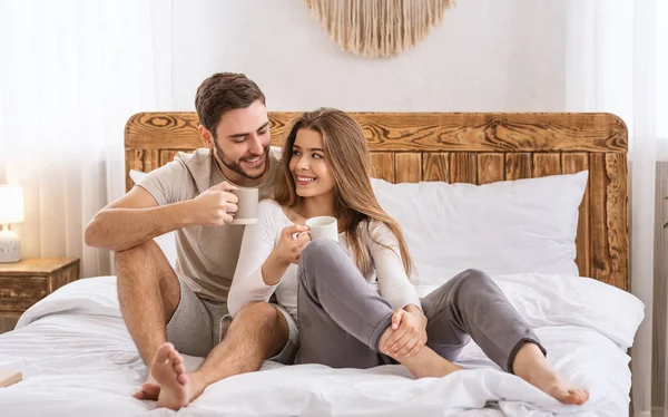 Счастливая пара в спальне на кровати и напитки из чашек — стоковое фото