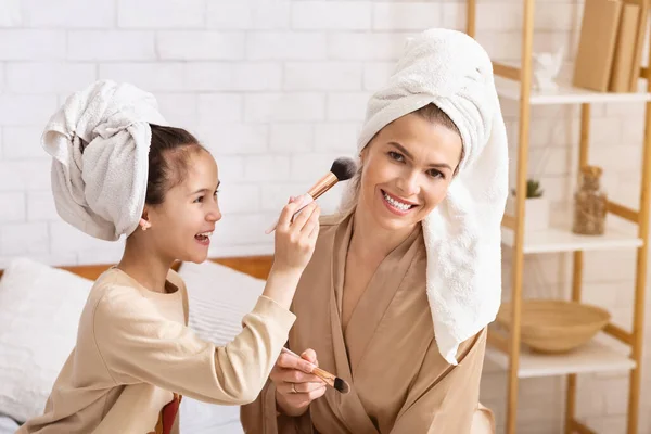 Salón de belleza en casa. Mamá e hija en toallas de baño divirtiéndose con maquillaje en interiores —  Fotos de Stock