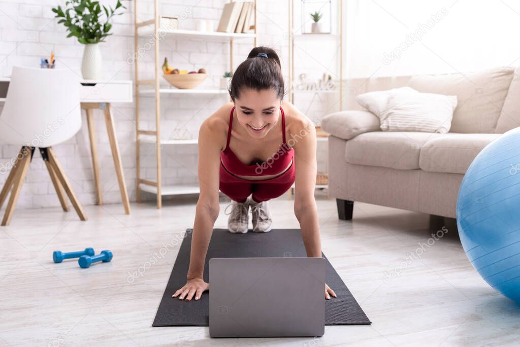 Active stay home pastimes. Millennial girl doing plank exercise to online video tutorial