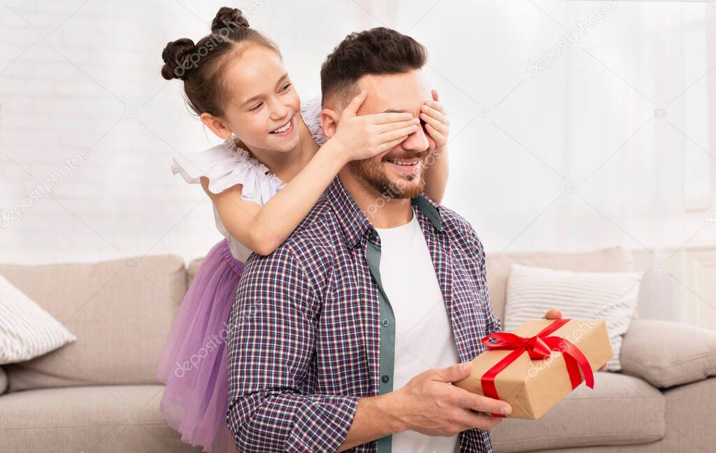 Happy daughter surprising her dad, closing his eyes and giving gift