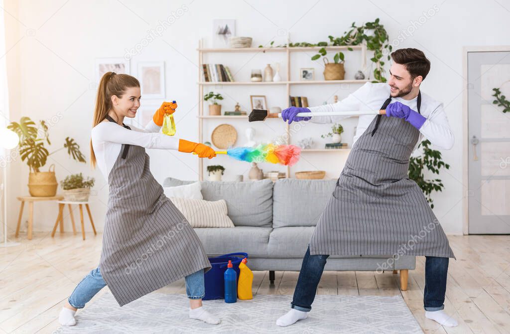 Guy and girl in aprons have fun, fight with spray, brush and broom.