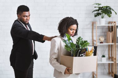 İşten atılma konsepti. Katı Afrikalı Amerikalı patron ve ofisinde bir kutu eşyası olan mutsuz kadın çalışan.