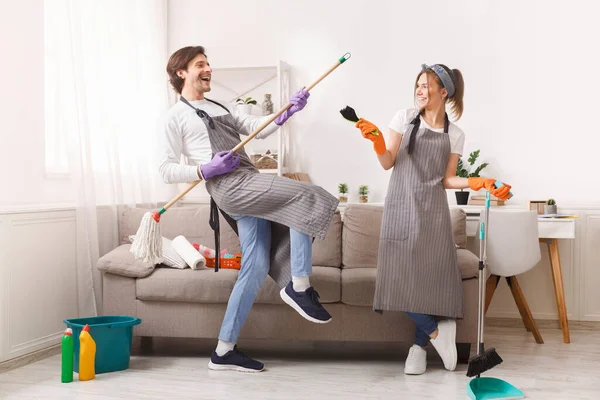 Casal alegre em aventais brincando com ferramentas domésticas enquanto Tidying Flat — Fotografia de Stock