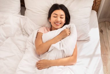 Dinlenmis Asyalı kadin evde yatakta uyaniyor.