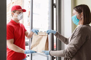 Koruyucu maskeli ve eldivenli kurye müşteriye dikkatlice paket verir