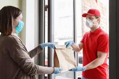 Coronavirus korumalı teslimatçı paketini tıbbi maskeli ve eldivenli müşteriye veriyor.