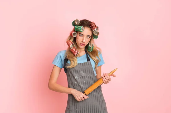 Strikte huisvrouw in schort met vlekken van bloem en deegroller in handen — Stockfoto