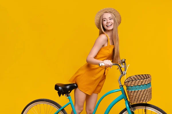 Beautiful young girl in summer clothes riding bike over yellow background — Stock Photo, Image