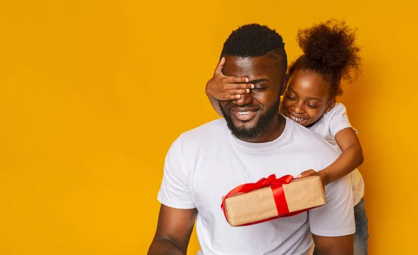 Vrolijk meisje feliciteert haar vader, sluit zijn ogen met geschenkdoos — Stockfoto