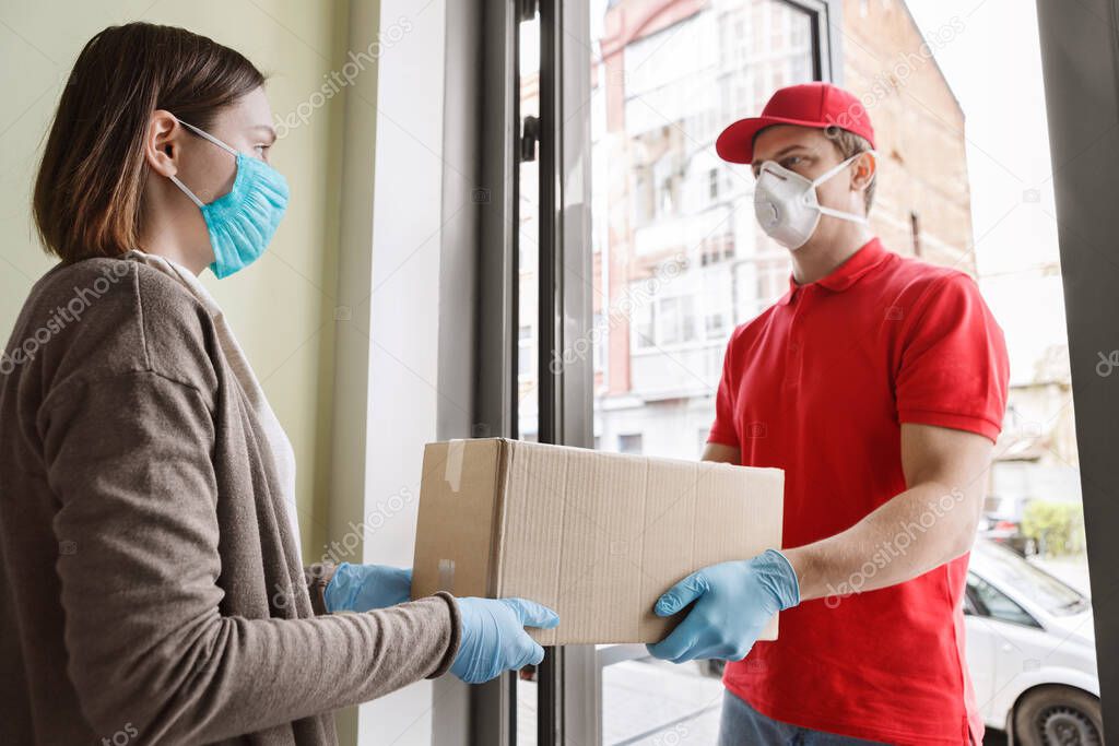 Courier delivery during quarantine. Girl opens door and takes parcel from deliveryman