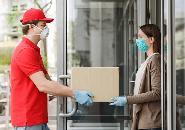 Ragazza apre la porta e prende scatola dal corriere, in maschera protettiva e guanti — Foto Stock