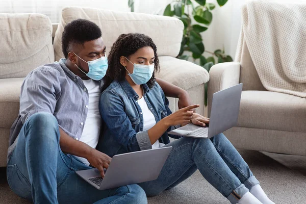 Trabajo remoto durante la pandemia. Pareja africana usando máscaras usando computadoras portátiles en casa —  Fotos de Stock