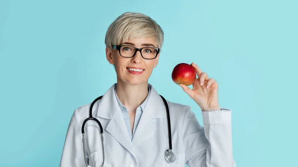 Gezond eten concept. Volwassen vrouw arts in bril houdt rode appel in de hand — Stockfoto