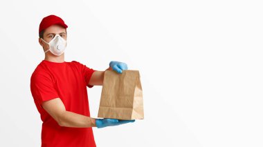 Tıbbi maskeli teslimatçı ve elinde kağıt torba tutan eldiven beyaz arka planda izole edilmiş, stüdyo fotoğrafı.