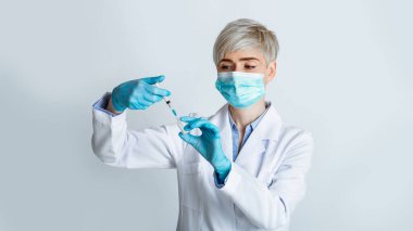 Tıbbi maskeli kadın doktor iğne yapmak için şırıngayı aldı.