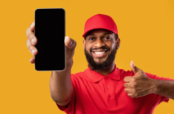 Homem de entrega mostrando a tela do celular que gere polegares-para cima, fundo amarelo, Mockup — Fotografia de Stock