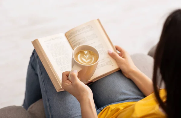 Rimani a casa a divertirti. Donna irriconoscibile godendo di caffè caldo e la lettura di libro emozionante, al chiuso — Foto Stock