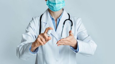 Dezenfeksiyon konsepti. Koruyucu maskeli doktor ellerini antiseptikle ovuyor.