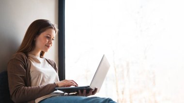 Kadın uzaktan kumandalı ev bilgisayarı pencere pervazında oturuyor.