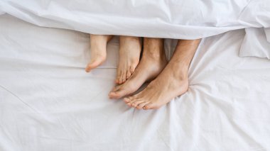 Yatakta sevgili bir çift. Dişi bacaklar erkek bacakları okşuyor.